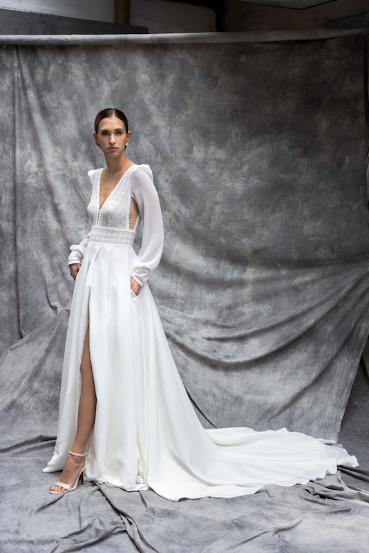 In questa foto una modella posa con un abito da sposa scivolato, maniche lunghe e tagli cut out in vita, stile boho. Il modello è della collezione Cymbeline e fa parte dei 100 abiti da sposa 2024 più belli