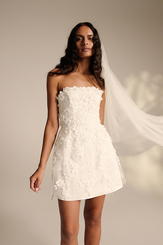 In questa foto una modella indossa un mini dress con applicazioni floreali ton sur ton in rilievo di Kaviar Gauche. Il vestito fa parte dei 100 abiti da sposa 2024 più belli