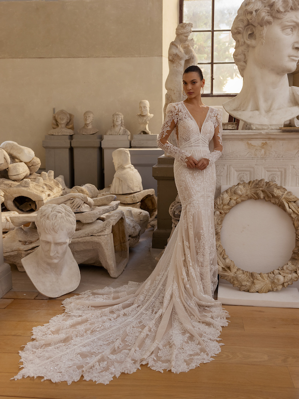 In questa foto una modella posa con una sirena in pizzo boho, maniche lunghe e coda, di Modeca: il vestito è tra i 100 abiti da sposa 2024 più belli
