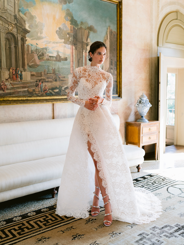 In questa foto una modella indossa un abito da sposa interamente in pizzo, con collo alto e maniche lunghe, di Monique Lhuillier 2024