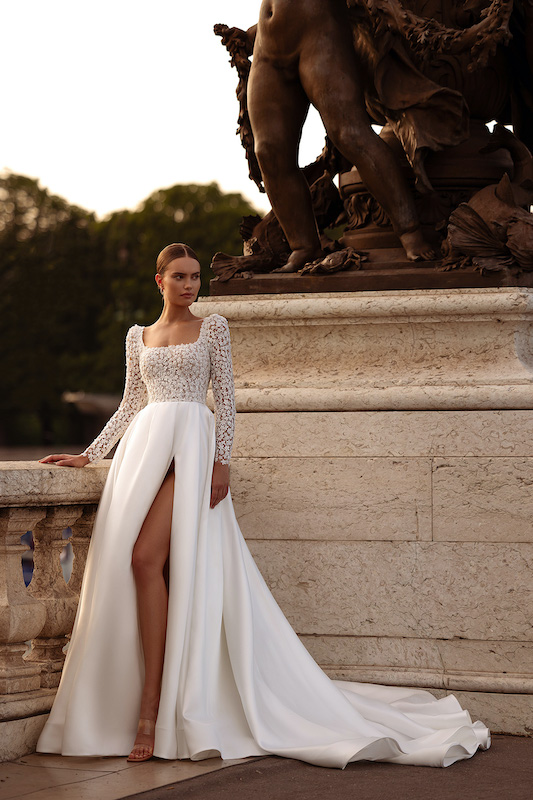 In questa foto una modella posa con un abito da sposa con scollatura quadrata di Oliver Martino 2024