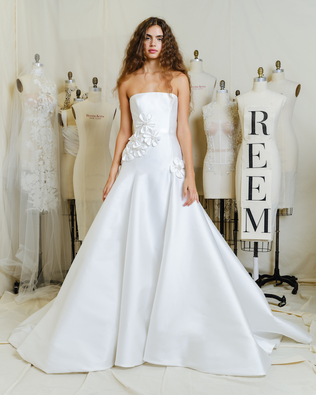 In questa foto una modella posa indossando un abito da sposa 2024 in mikado di seta bianco ottico di Reem Acrea