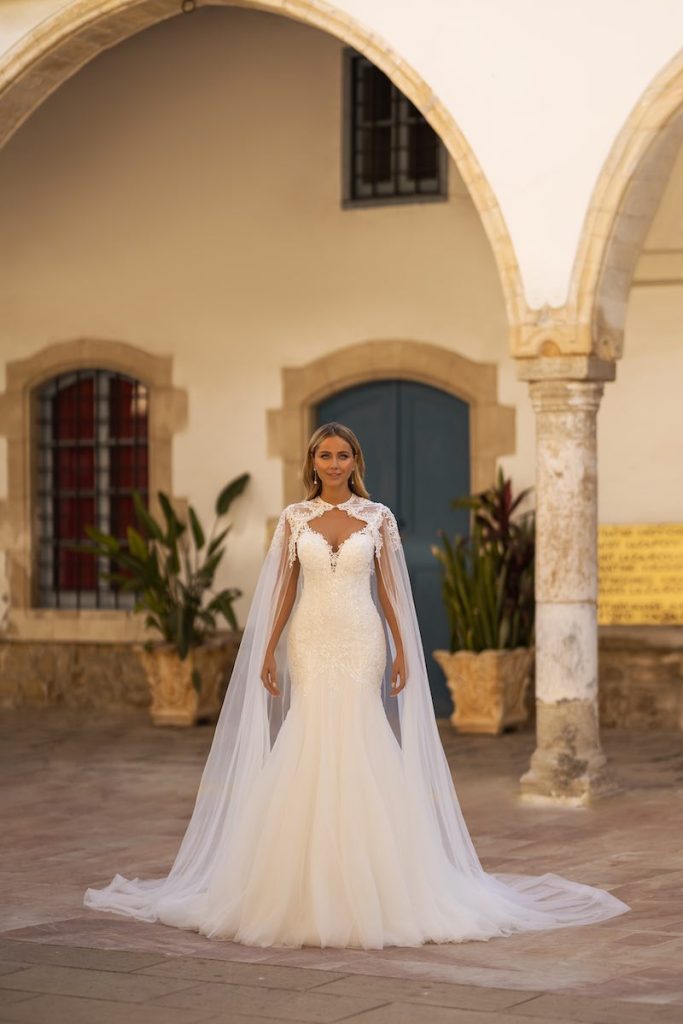 In questa foto una modella indossa un abito da sposa a sirena Daniela Di Marino 2024 con cappa staccabile