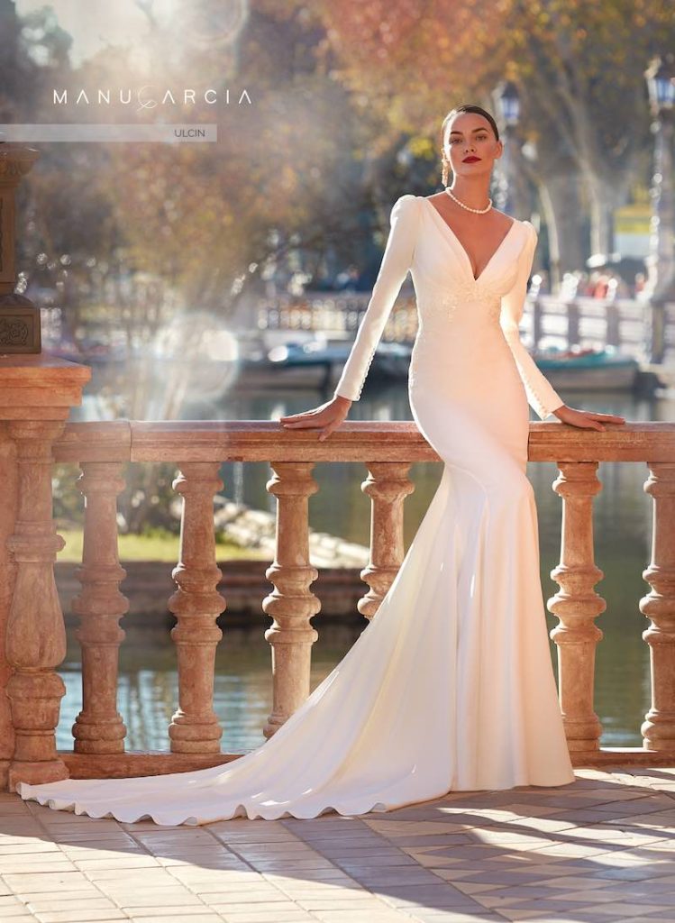 In questa foto una modella indossa uno dei modelli di abiti da sposa a sirena 2024 di Manu Garçia in tessuto  minimal con scollo a V, maniche e lungo strascico