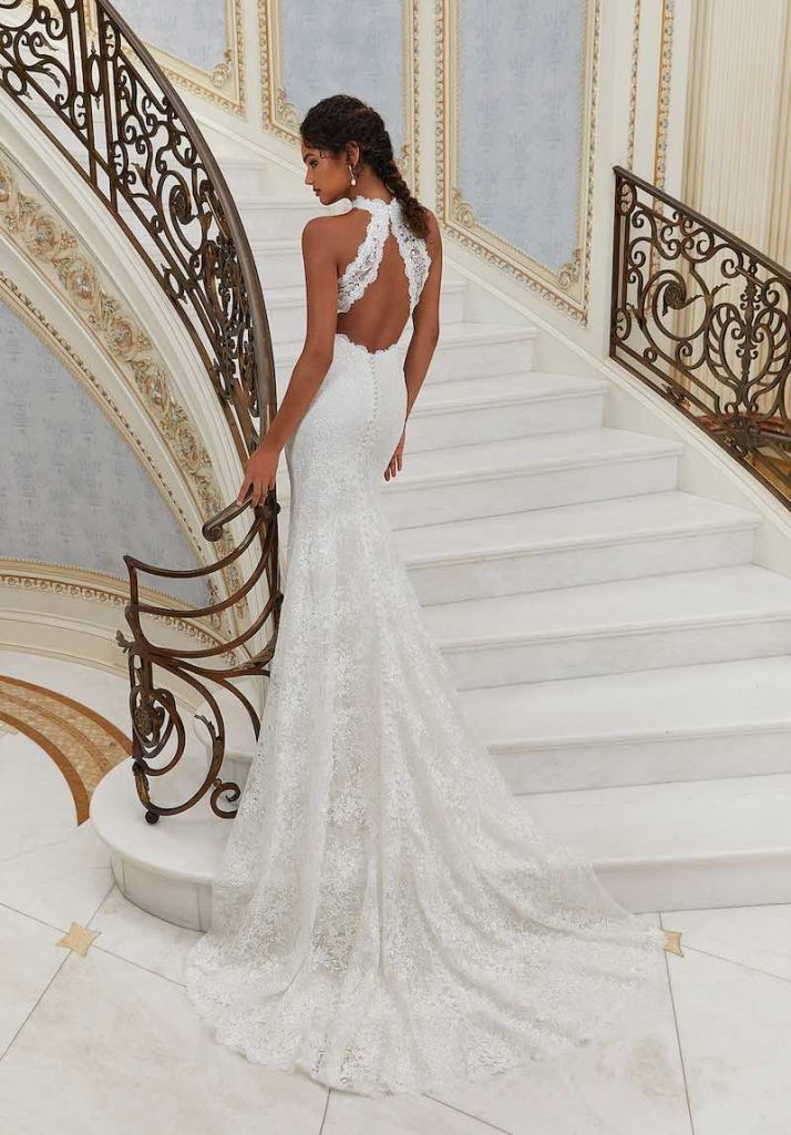 In questa foto una modella di spalle sulle scale indossa un abito da sposa a sirena in pizzo con scollatura ad oblò sulla schiena di Morilee