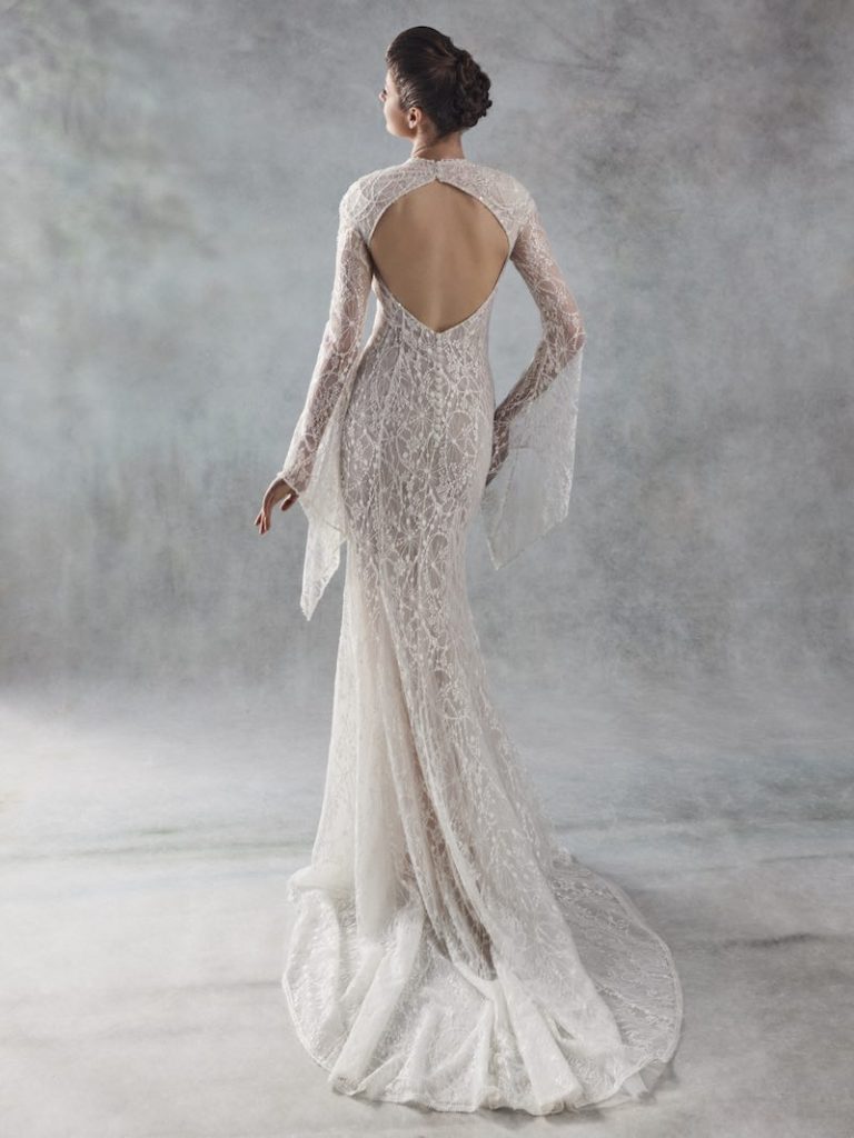 In questa foto una modella  di spalle indossa un abito da sposa a sirena in pizzo con maniche e scollatura ad oblò sulla schiena di Otilia Brailoiu
