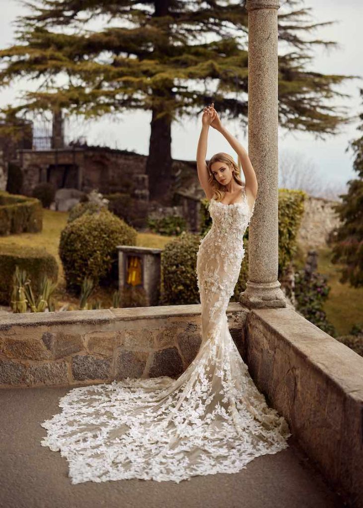 In questa foto una modella indossa un abito da sposa a sirena Randy Fenoli 2024 con microfiori 3D all-over e lungo strascico