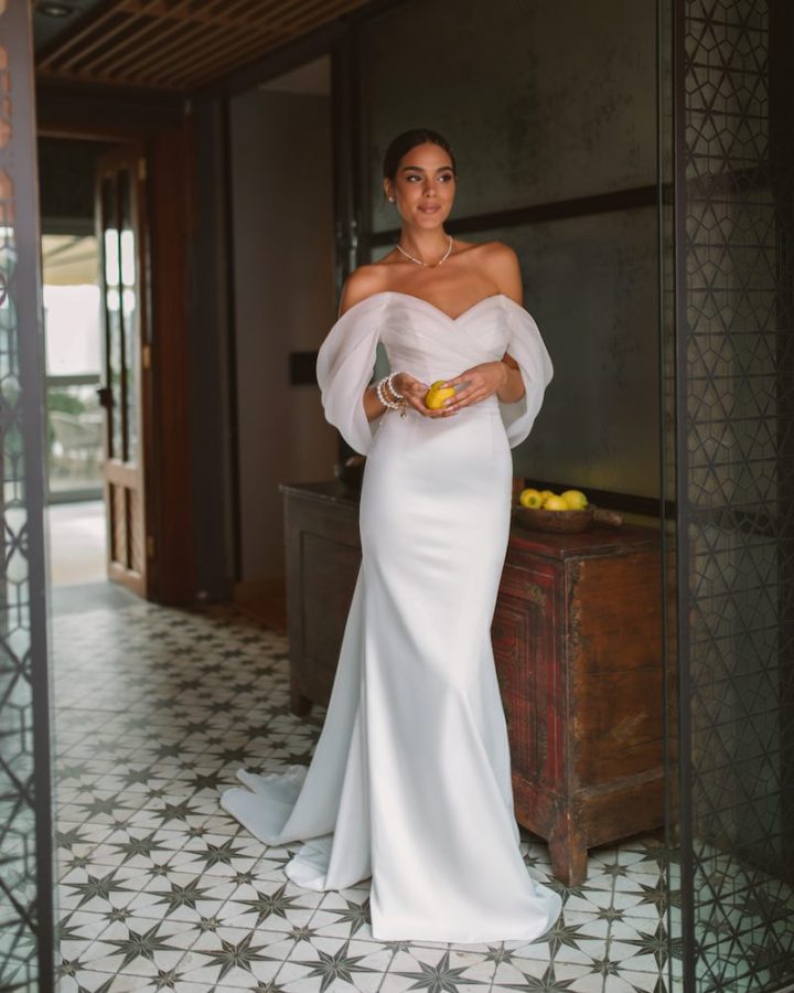 In questa foto una modella indossa uno dei modelli di abiti da sposa a sirena 2024 di Rara Avis con scollatura off shoulder