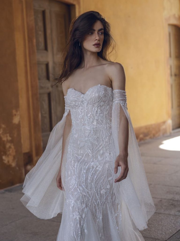 In questa foto una modella indossa un abito da sposa Ricca Sposa 2024 con dettagli gioiello, scollo a cuore e maniche rimovibili
