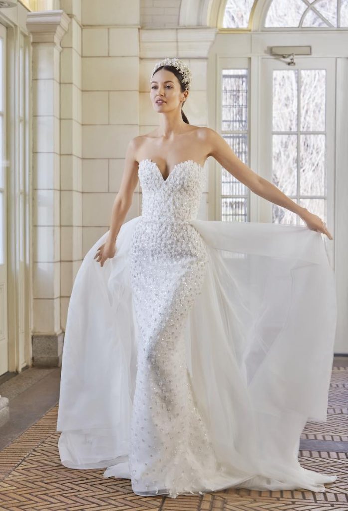 In questa foto una modella indossa uno dei modelli di abiti da sposa a sirena 2024 con microfiori 3D di Sareh Nouri con sopragonna staccabile in chiffon
