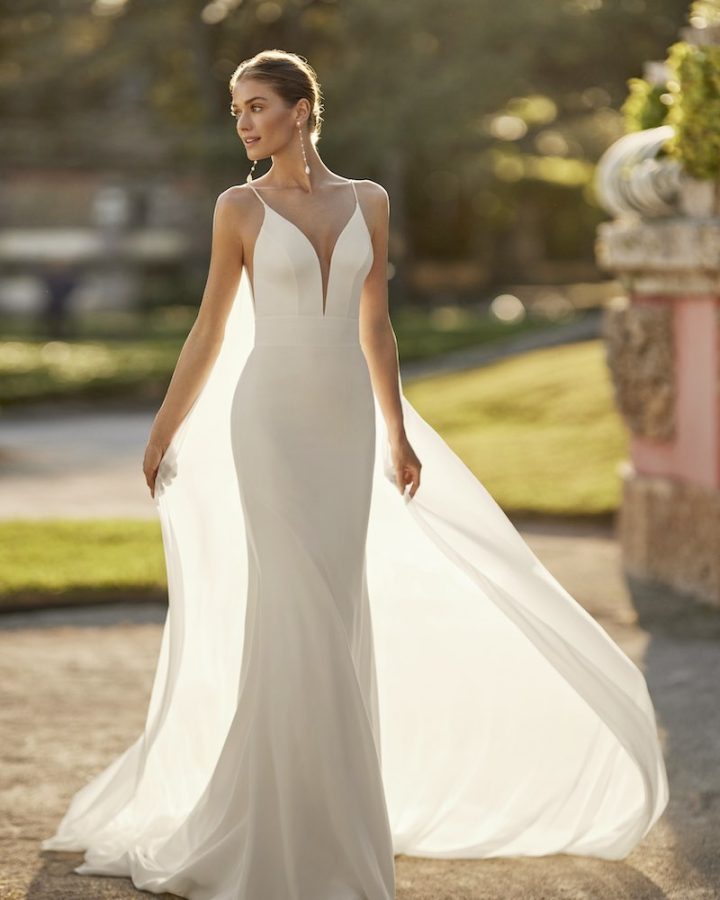 In questa foto una modella indossa uno dei modelli di abiti da sposa a sirena 2024 di Aire Barcelona con scollo a V e velo rimovibile 