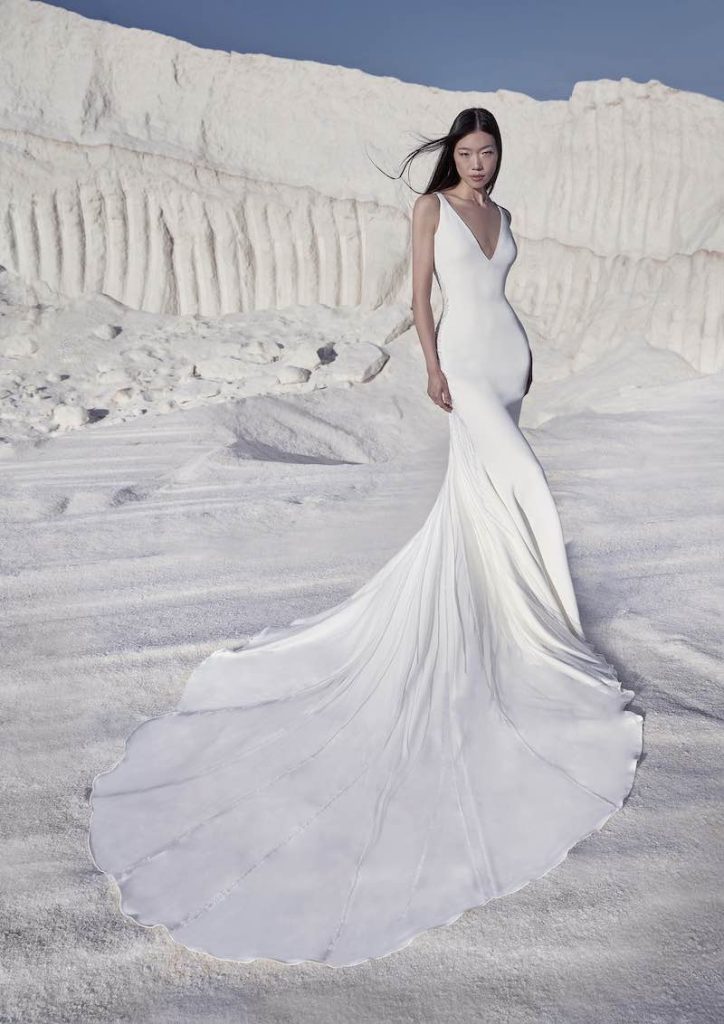 In questa foto una modella indossa uno dei modelli di abiti da sposa a sirena 2024 Atelier Pronovias con scollo a V e lungo strascico
