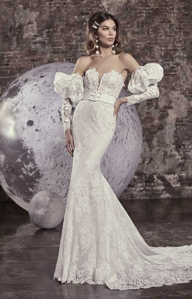 In questa foto una modella indossa uno dei modelli di abiti da sposa a sirena 2024 di Elisabetta Polignano in pizzo, maniche balloon rimovibili e cintura in vita con logo della stilista
