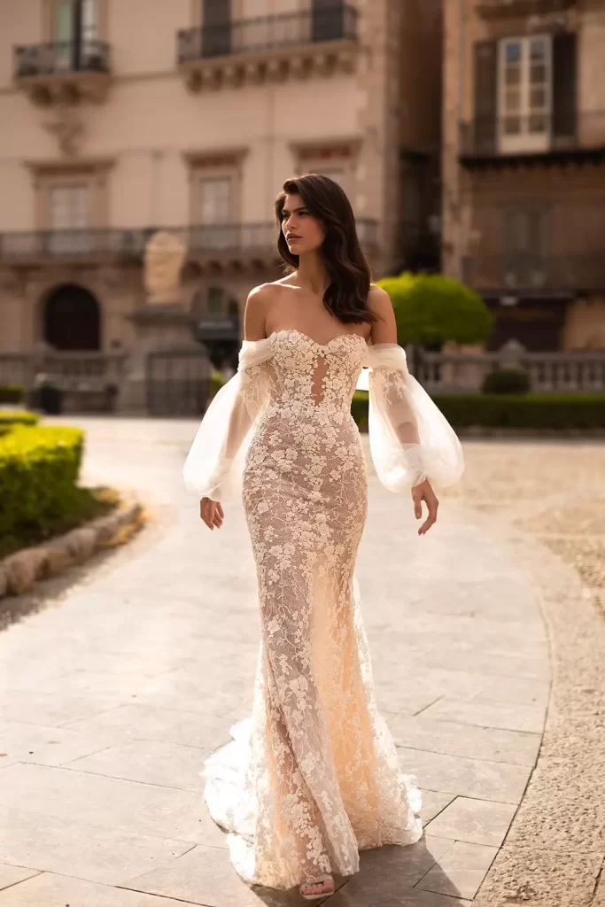 In questa foto una modella indossa uno dei modelli di abiti da sposa a sirena 2024 di Eva Lendel in pizzo e tulle e maniche balloon rimovibili