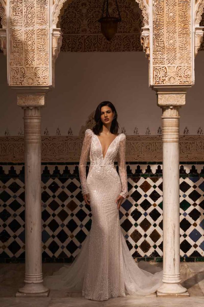 In questa foto una modella indossa un abito da sposa a sirena Wonà Concept 2024 con scollo a V, maniche e dettagli sparkling all over
