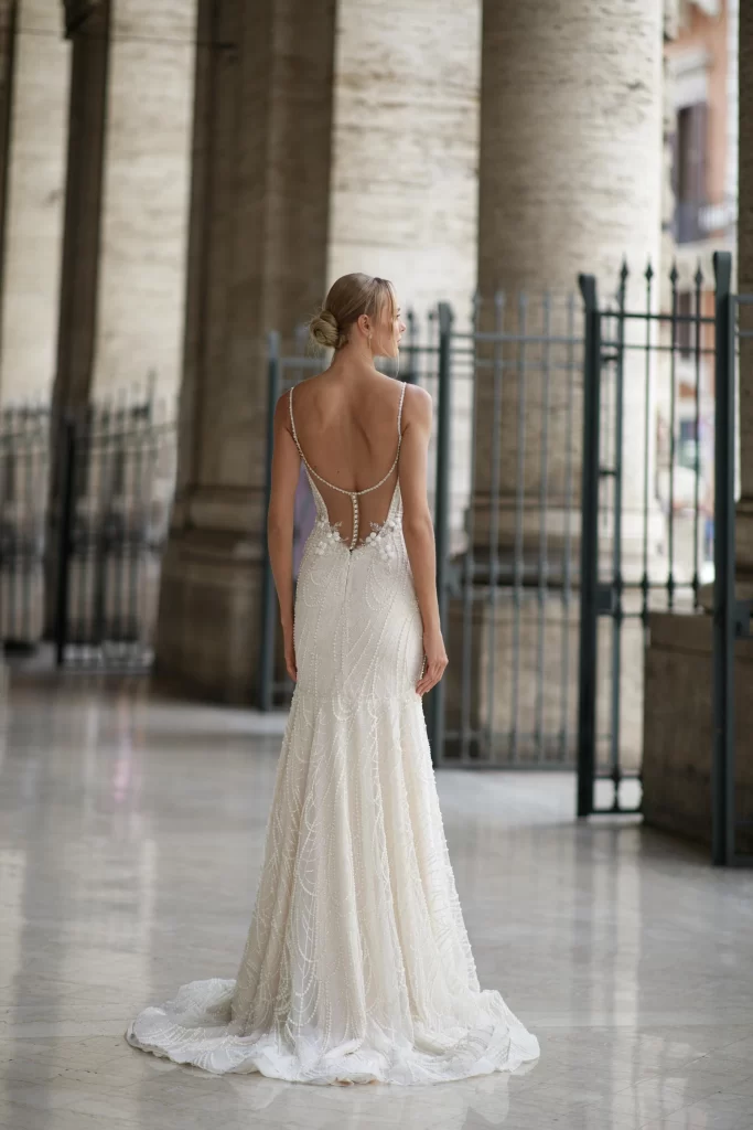 In questa foto una modella  di spalle indossa un abito da sposa a sirena in pizzo con scollatura sulla schiena di Yedina Wedding Studios