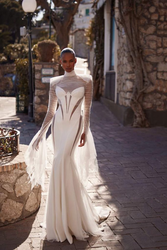 In questa foto una modella indossa un abito da sposa a sirena Julie Vino con cut out geometrici su busto e lunghezze e maniche in tulle leggerissimo