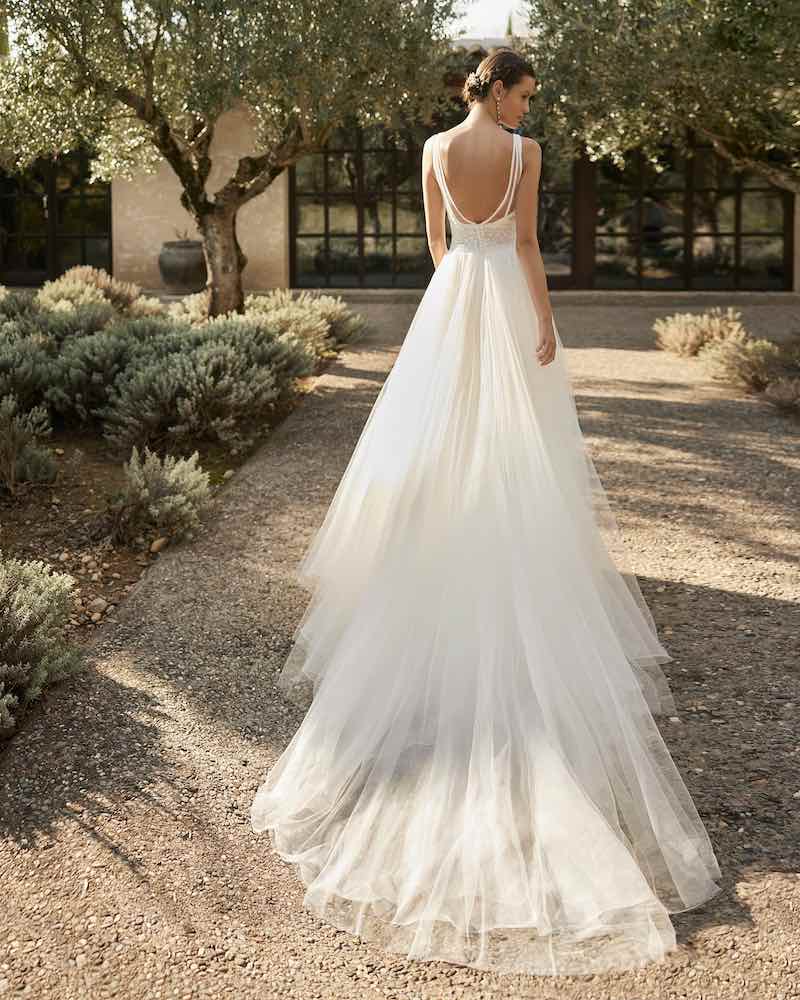 In questa foto una modella inquadrata di spalle indossa un abito da sposa con gonna in tulle, strascico e scollatura ovale sulla schiena