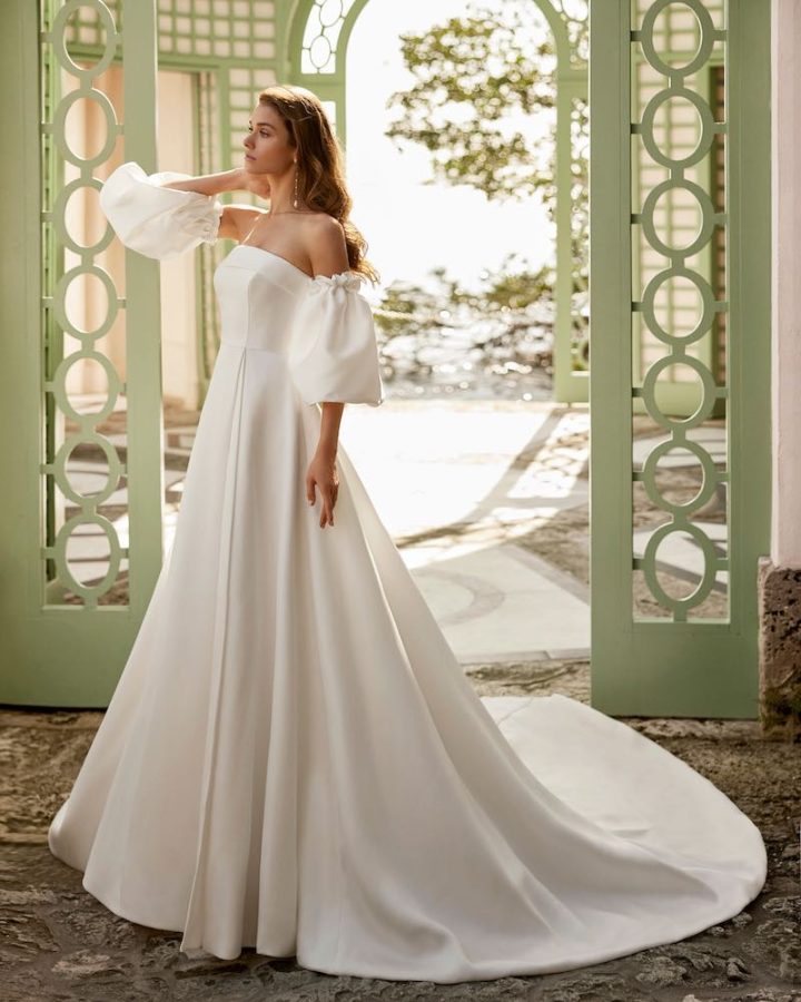 In questa foto una modella indossa uno degli abiti da sposa Aire Barcelona 2024 in mikado con gonna ad A, strascico e maniche balloon staccabili