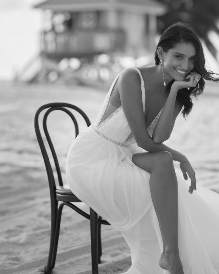 In questa foto in bianco e nero posa seduta su una sedia sulla spiaggia indossando un abito da sposa modello scivolato con corpetto con scollo a V