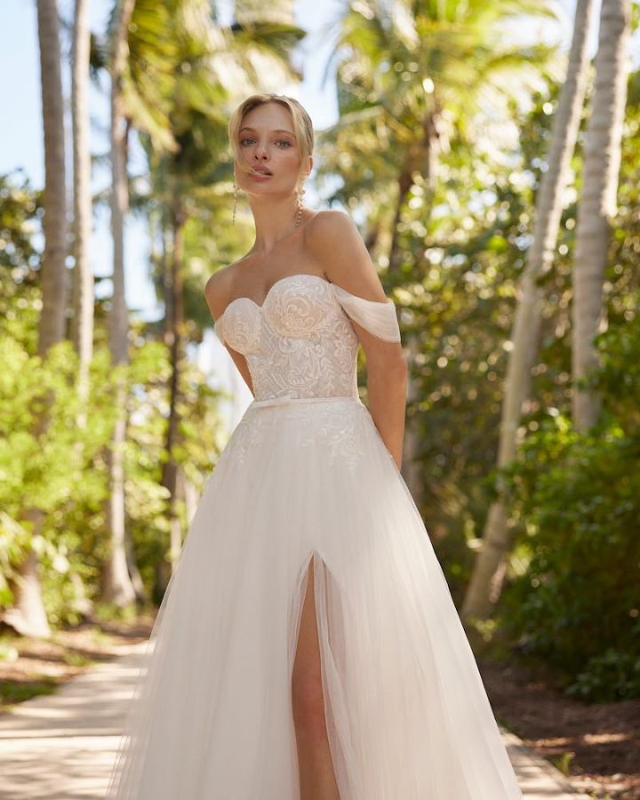 In questa foto una modella posa indossando un abito da sposa 2024 con gonna in tulle con spacco, scollo a cuore e cintura con microfiocco in vita