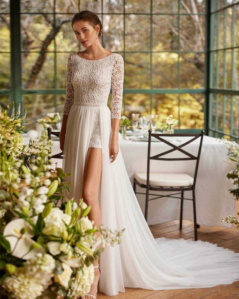 In questa foto una modella posa indossando un abito da sposa trasformabile con shorts, corpetto con maniche a tre quarti in pizzo floreale e sopragonna staccabile in chiffon