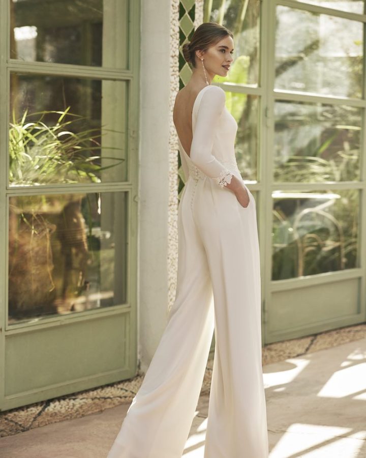 In questa foto una modella indossa una tuta da sposa con scollatura sulla schiena di Alma Novia