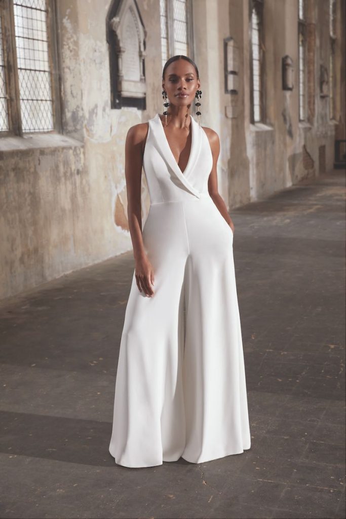 In questa una modella indossa uno degli abiti da sposa con pantaloni culotte 2024 della collezione Adore by Justin Alexander con scollo a V e revers sciallati