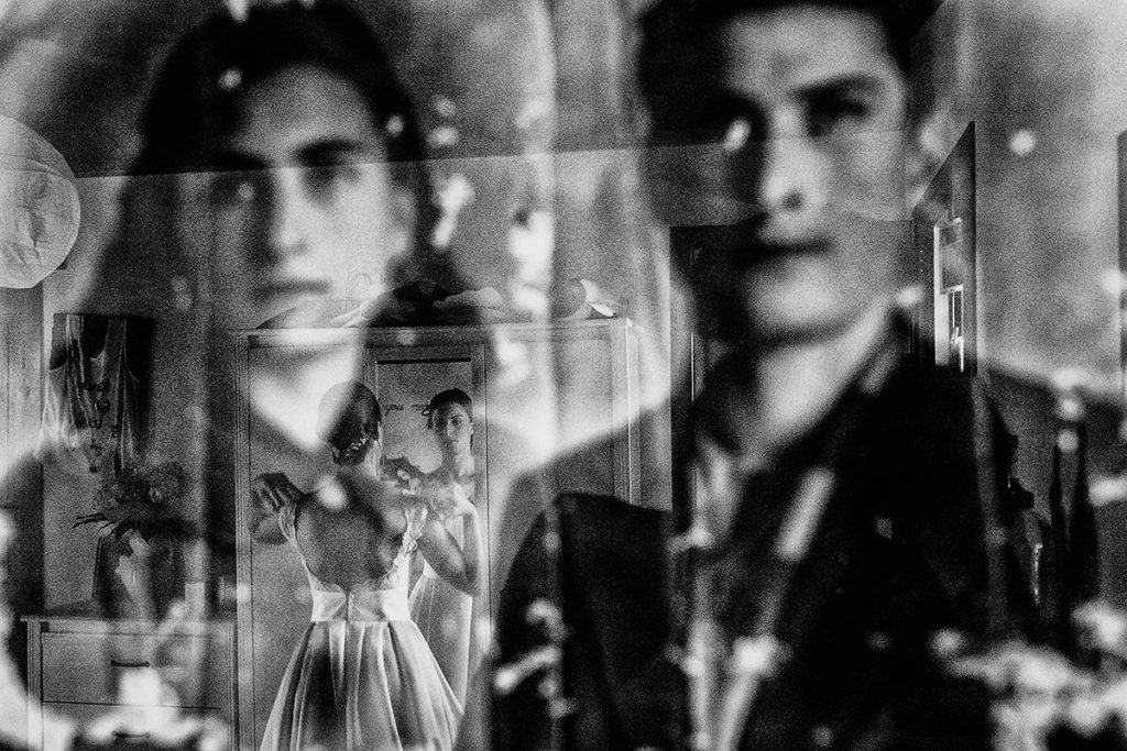 Nella foto in bianco e nero realizzata da Antonino Gitto il riflesso di una foto di famiglia dietro cui traspare una sposa durante i preparativi del matrimonio