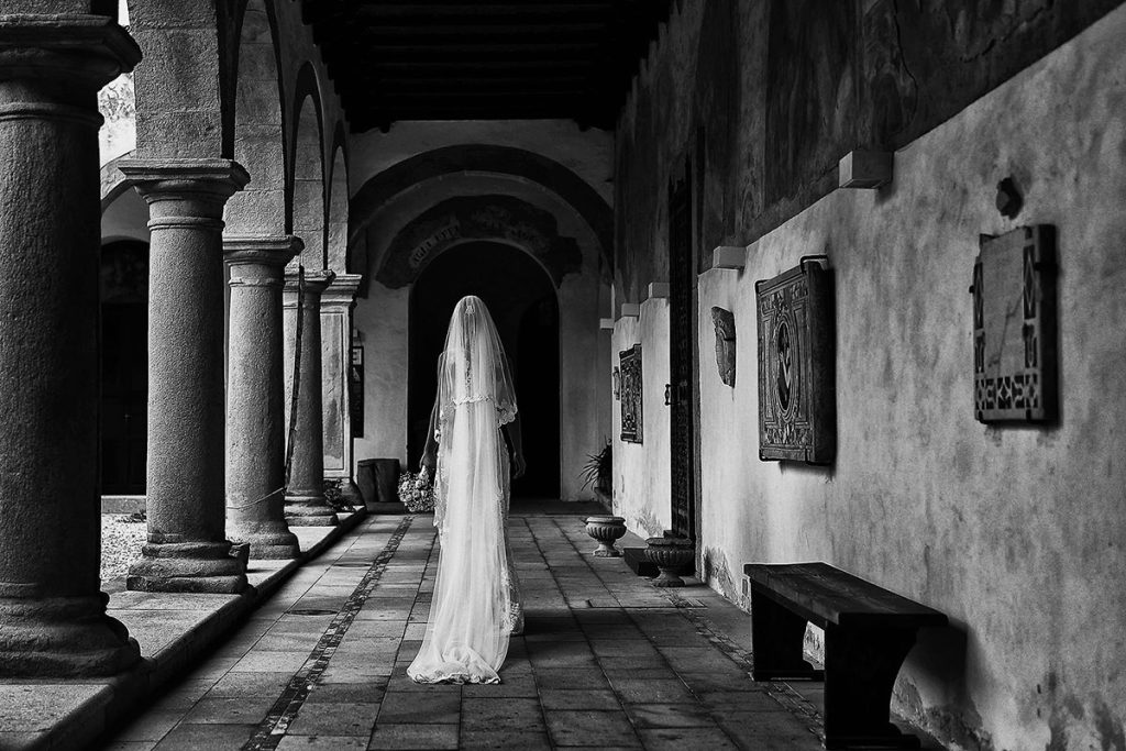 Nella foto in bianco e nero realizzata da Antonino Gitto una sposa di spalle cammina nel portico di una Chiesa in Sicilia