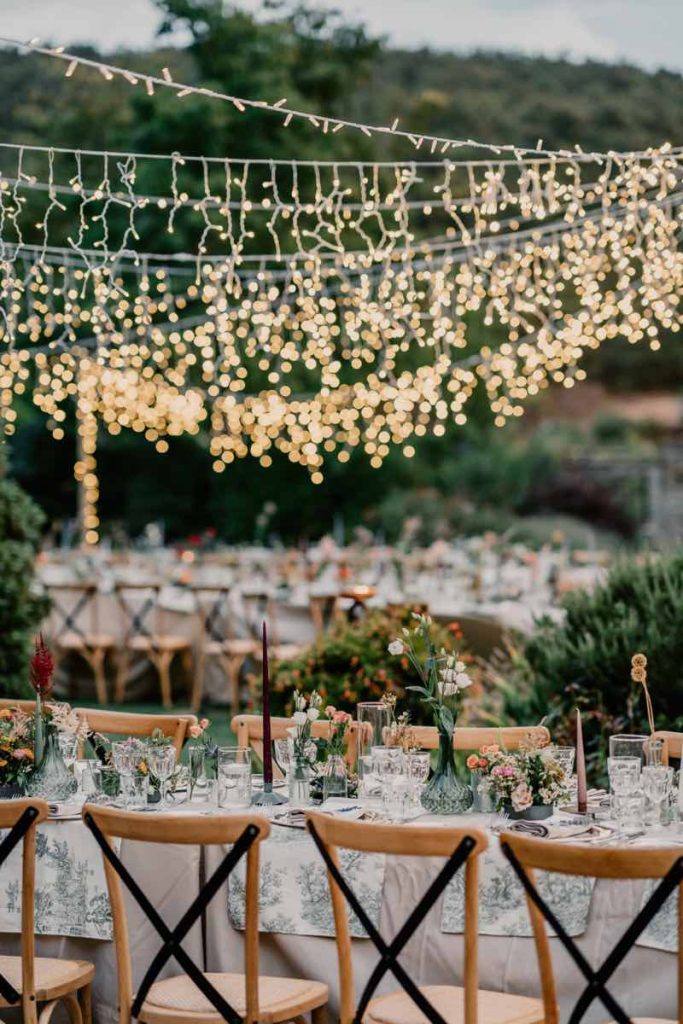 In questa foto di Claudio Fasci il dettaglio di un matrimonio in stile Country Chic realizzato con tavoli imperiali, sedie in legno, tovagliato e vasetti di colore verde e bianco e un tetto di luci
