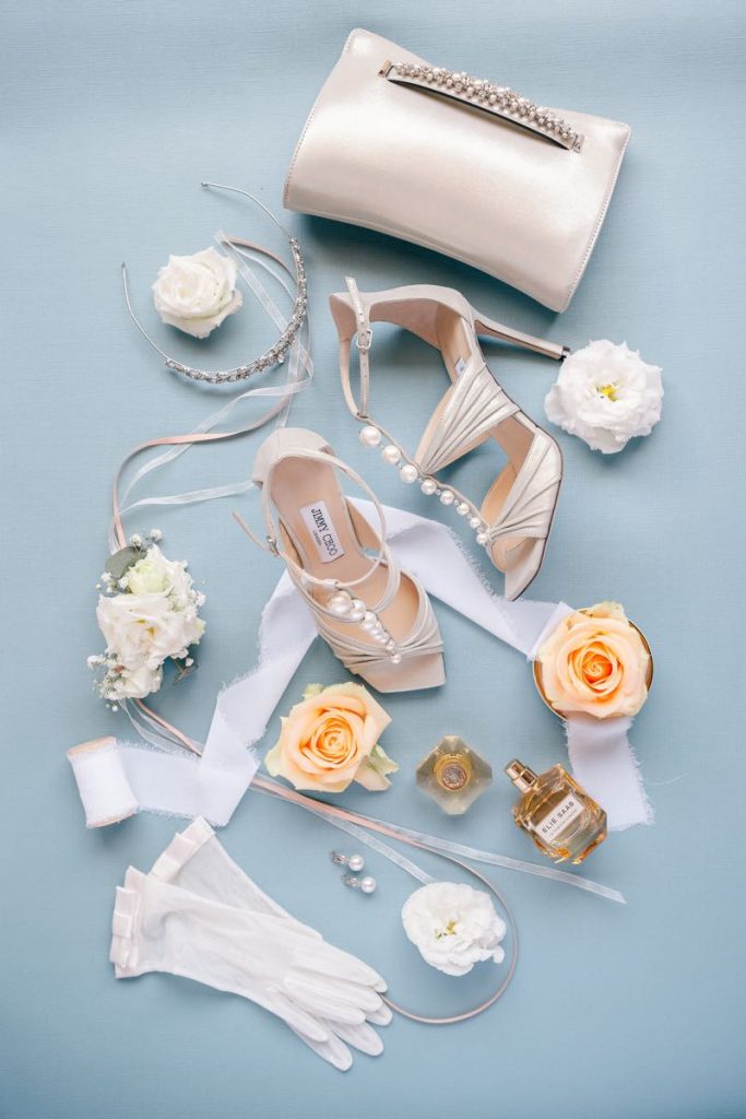 In questa foto di Claudio Fasci scattata dall'alto tutti gli accessori di una sposa: guanti corti, profumo, orecchini di perle, cerchietto gioiello, clutch e sandali Jimmy Choo