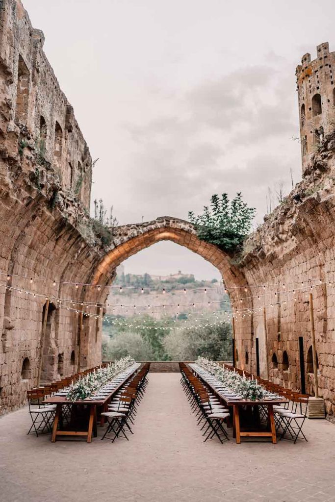 In questa foto di Claudio Fasci il ricevimento in stile Country Chic in un'antica chiesa sconsacrata all'aperto, allestita con due tavoli imperiali di legno nudo decorati con runner floreali