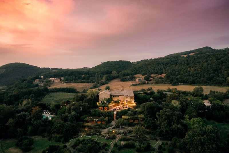 In questa foto scattata al crepuscolo con un drone una cascina illuminata da un tetto di luci e circondata dal verde