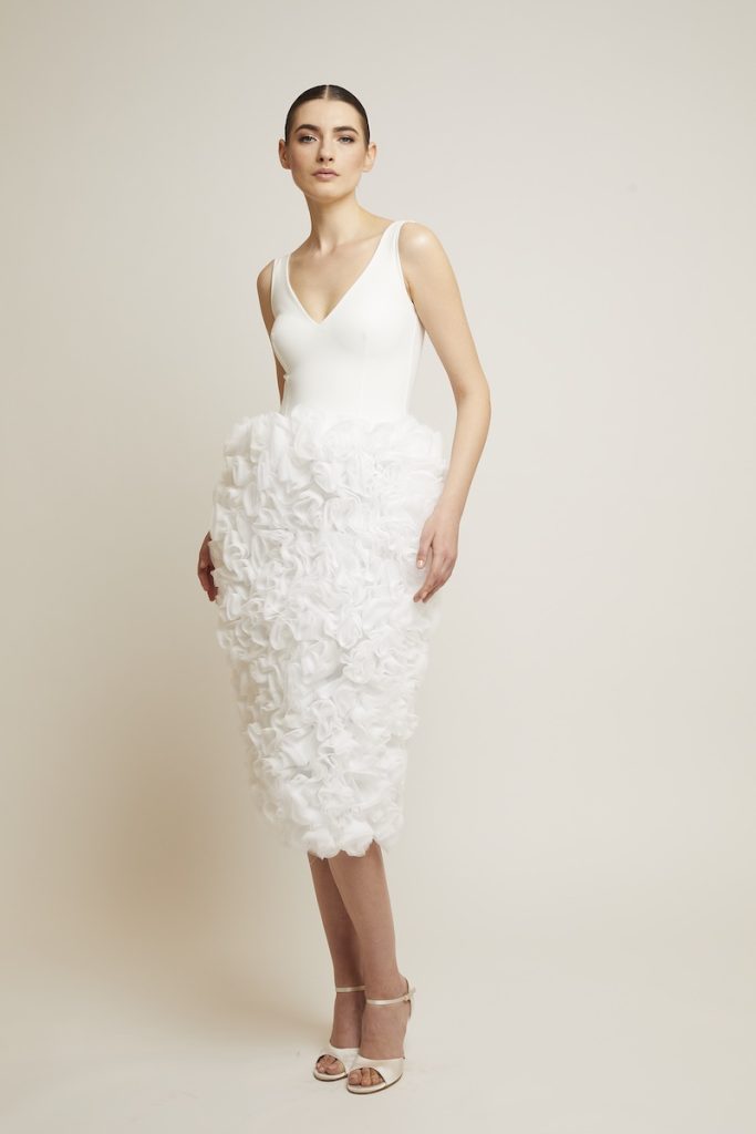 In questa foto una modella posa indossando uno degli abiti da sposa particolari 2024 corto di Chiara Boni con gonna a rose 3D