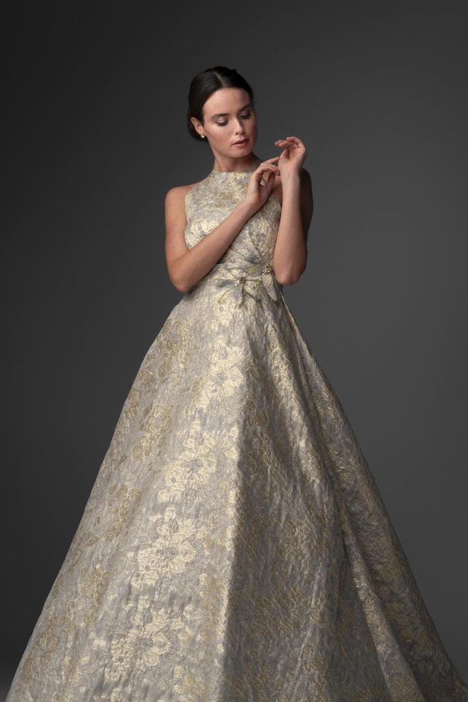 In questa foto una modella posa indossando uno degli abiti da sposa particolari 2024 di Chiara Vitale in tessuto damascato di colore oro