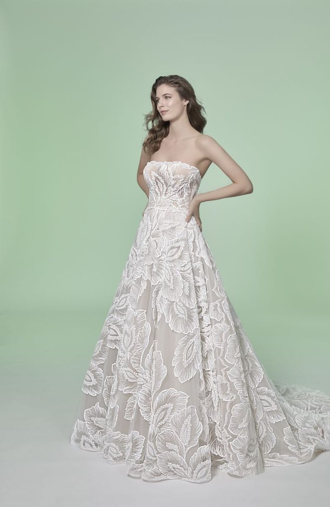 In questa foto una modella posa indossando un abito da sposa ampio con alternanza di stoffe diverse a motivi floreali di Couture Fe