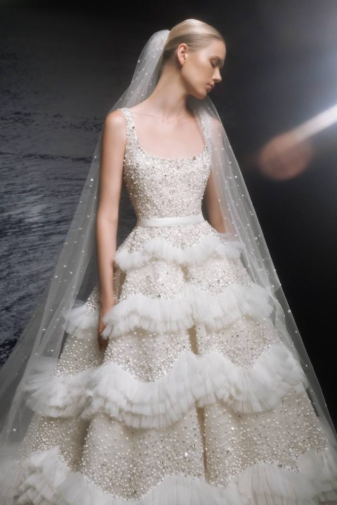 In questa foto una modella posa indossando uno degli abiti da sposa particolari 2024 modello principessa con balze di Elie Saab