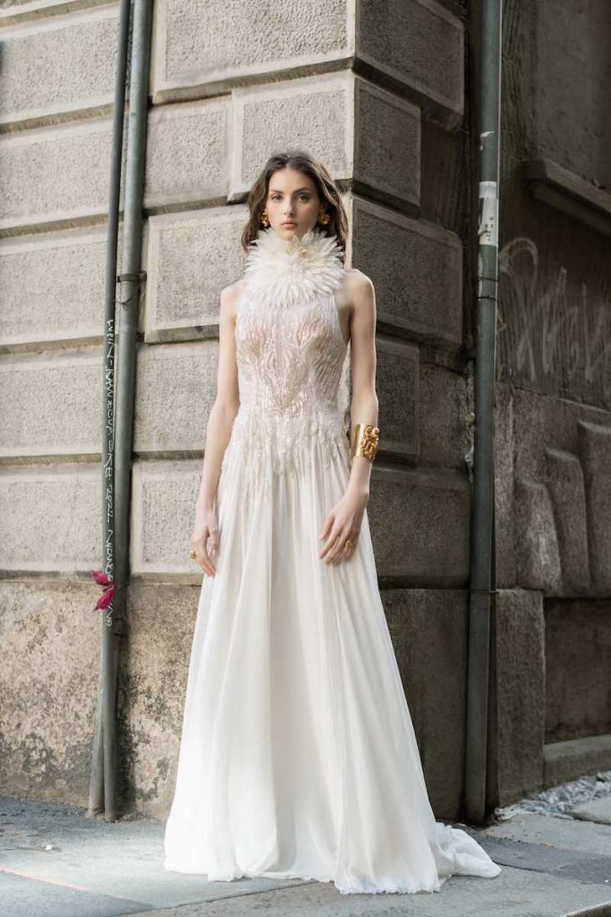 In questa foto una modella posa indossando uno degli abiti da sposa particolari 2024 Le Fate Milano con dettaglio floreale sul collo