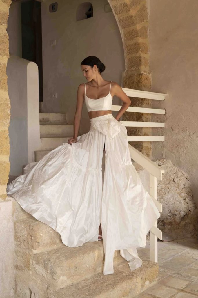 In questa foto una modella posa indossando uno degli abiti da sposa particolari 2024 con crop top con maxi ruches sul punto vita
