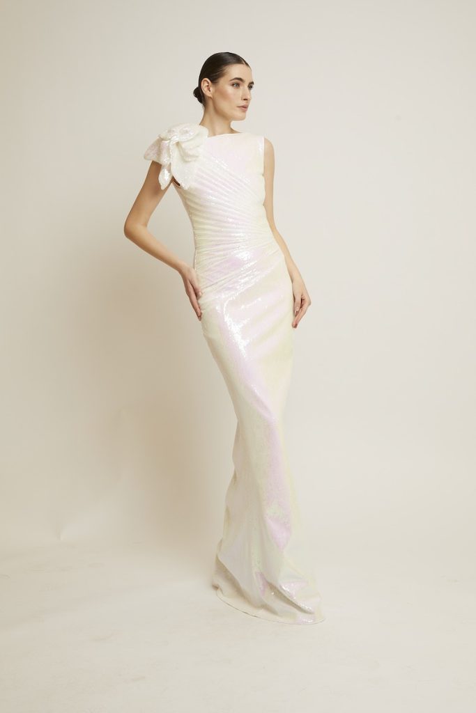 In questa foto una modella posa indossando uno degli abiti da sposa particolari 2024 di Chiara Boni con maxi fiore 3D sulla spalla destra