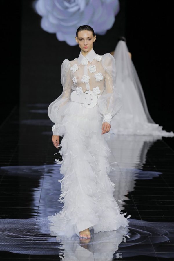 In questa foto una modella sfila indossando un abito da sposa con plumage sulla gonna e maxi cintura di Isabel Sanchis