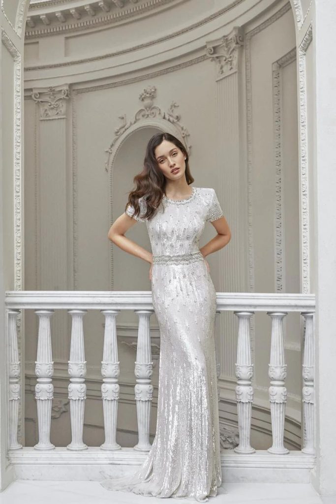 In questa foto una modella posa indossando uno degli abiti da sposa particolari 2024 di Jenny Packham a sirena con ricami di colore argento