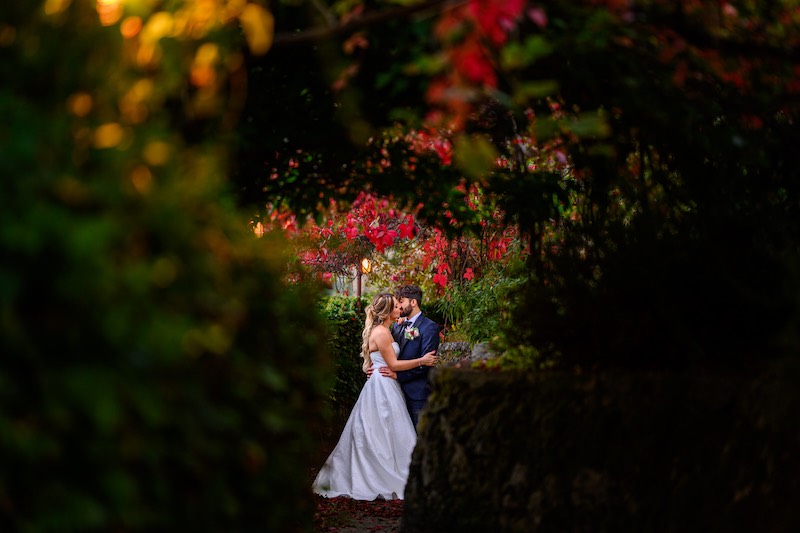 In questa foto due sposi si abbracciano e si baciano in un giardino fiorito