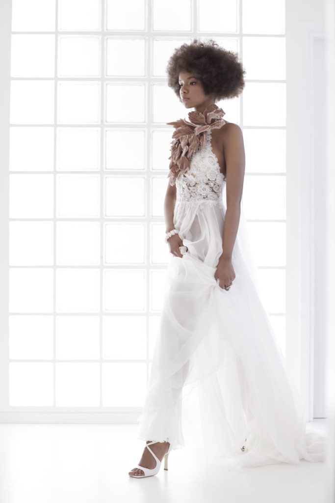 In questa foto una modella indossa un abito da sposa Le Fate Milano Couture con maxi fiori 3D al collo e corpetto con fiori ricamati. La modella indossa anche un paio di sandali da sposa