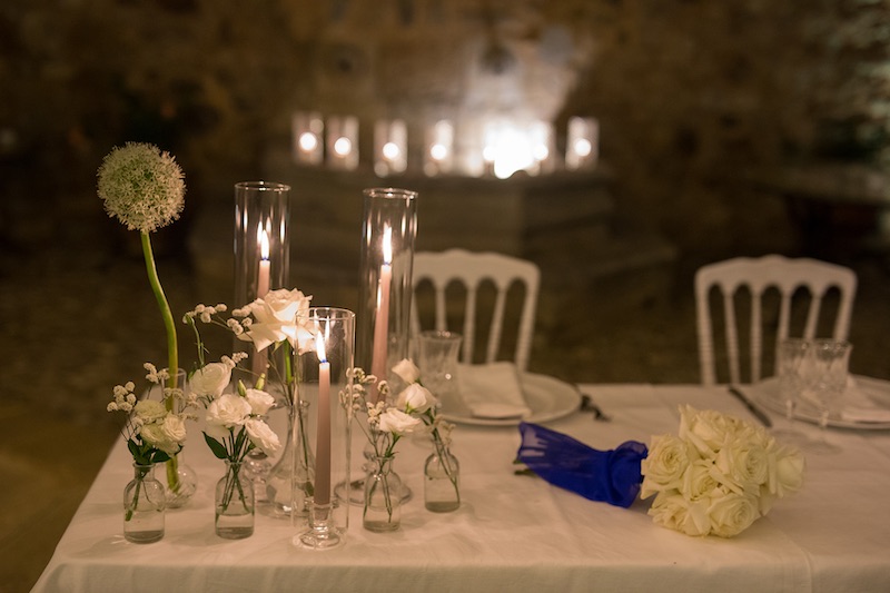 In questa foto un dettaglio della mise en place del matrimonio di Lucio e Federica realizzata dalla Wedding Planner Antonella Candido con candele di colore bianco, portacandele in vetro e fiori di colore bianco. In primo piano è inquadrato anche il bouquet della sposa