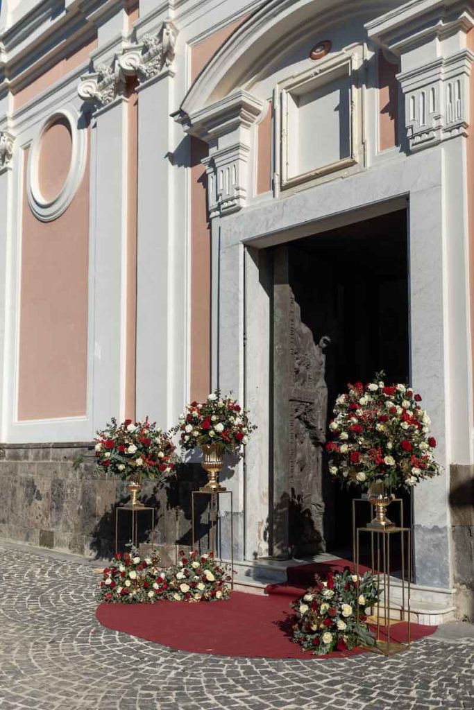 In questa foto l'allestimento floreale dell'ingresso della chiesa del matrimonio di Matteo e Pina realizzato dal Wedding Planner Stefano Miranda con composizioni di rose di colore rosso e bianco, bacche, pungitopo, eucalipto e pino