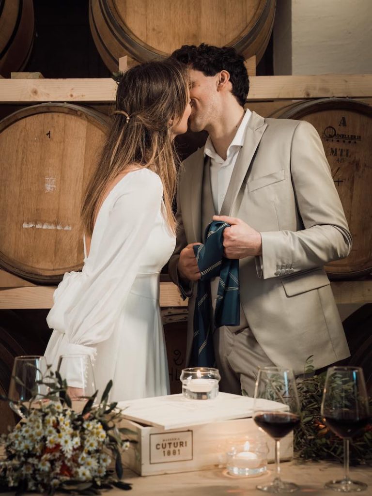 In questa foto due sposi si baciano davanti alle botti della cantina di Masseria Cuturi