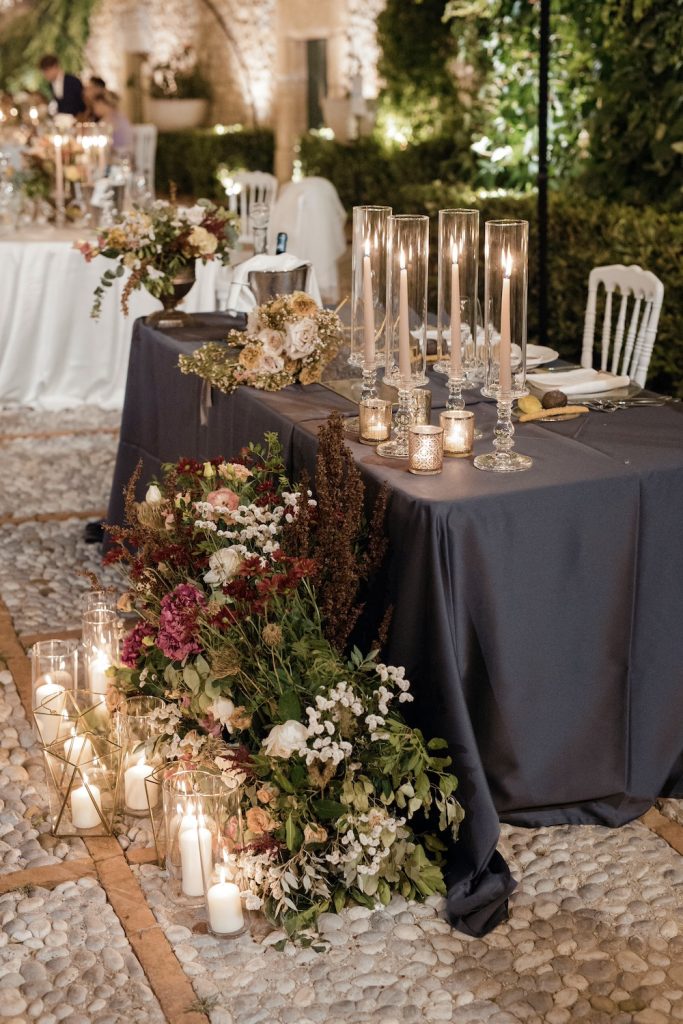 In questa foto un tavolo degli sposi allestito con candele, tea light, fiori bordeaux e tovagliato grigio antracite