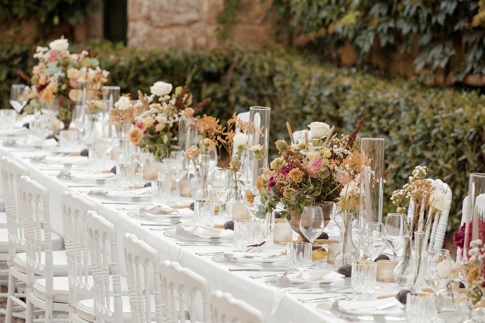 In questa foto un tavolo imperiale allestito con coppe di fiori di colore bordeaux e rose Playa e rose cappuccino